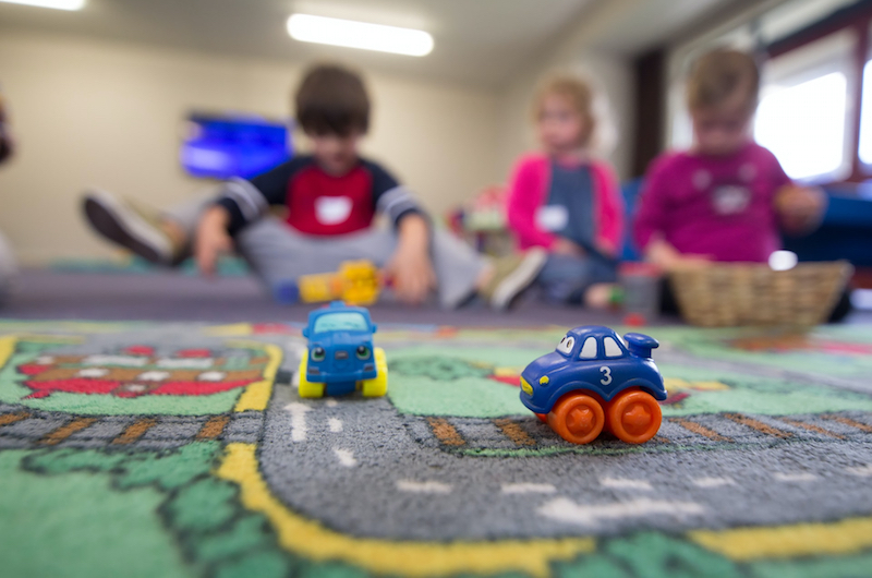 Spielteppich mit zwei Autos.Drei kleine Kinder unscharf im Hintergrund.